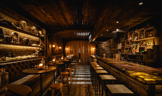 Perspective view of a pirate-themed bar interior, showcasing the contrast between the glowing bar counter on the right and the intimate, candlelit sea