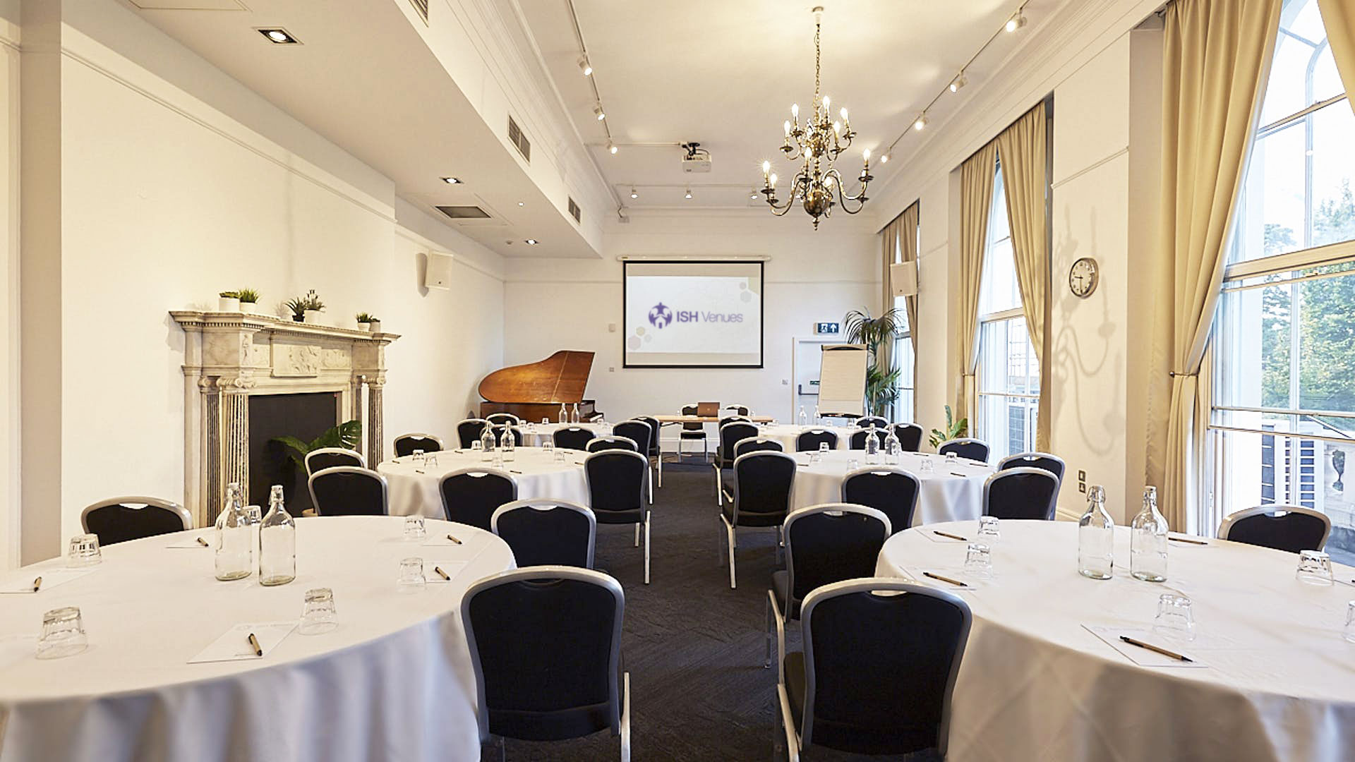 Spacious event space at ISH Venues with cabaret seating, high ceilings, a projector screen, and traditional architectural features.