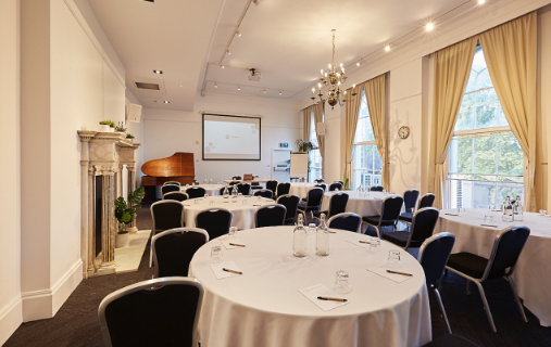 The Gulbenkian configured in cabaret style with a grand piano, marble fireplace, chandelier, and natural light from windows.