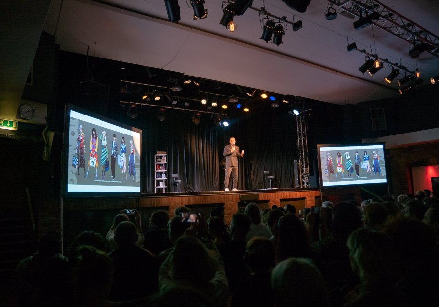 Live presentation at ISH Venues with a speaker on stage flanked by two large projection screens.