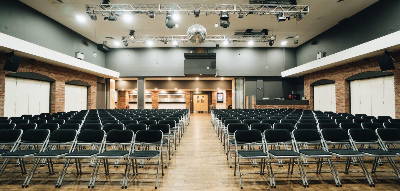 Symmetrical view of theater seating in Venue 1 at ISH Venues showing the industrial ceiling and lighting rig.
