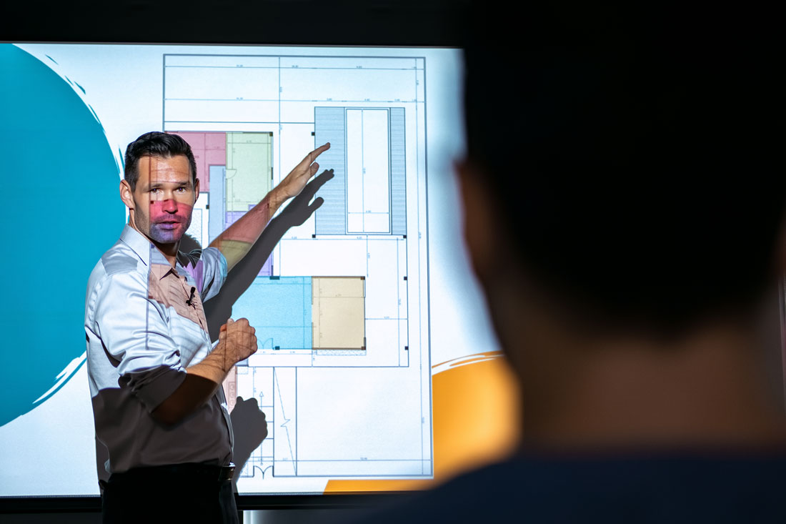 Professional presenter demonstrating architectural floor plans on a high-definition projector screen