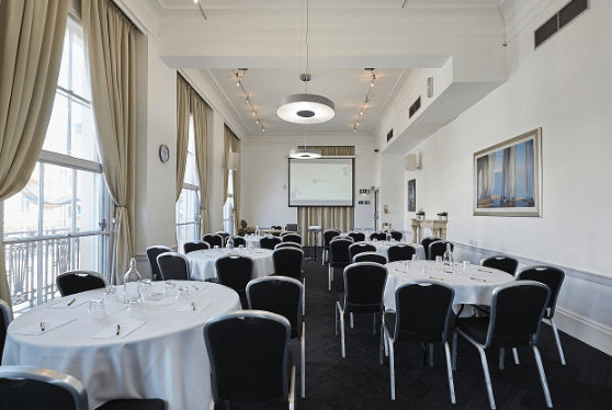 Versatile cabaret-style workshop layout featuring round tables, black stacking chairs, and a projector screen in a bright, airy space.