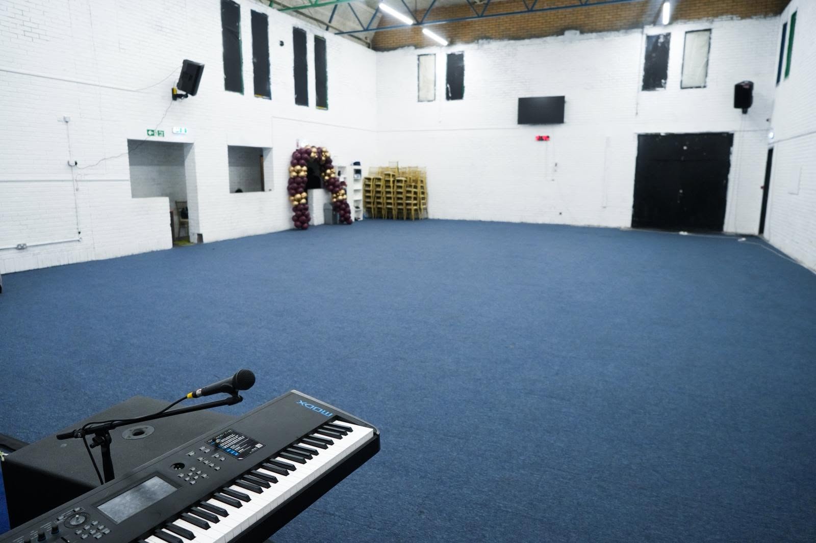 Large East London performance venue showcasing an on-stage keyboard, microphone, and open space for community events.