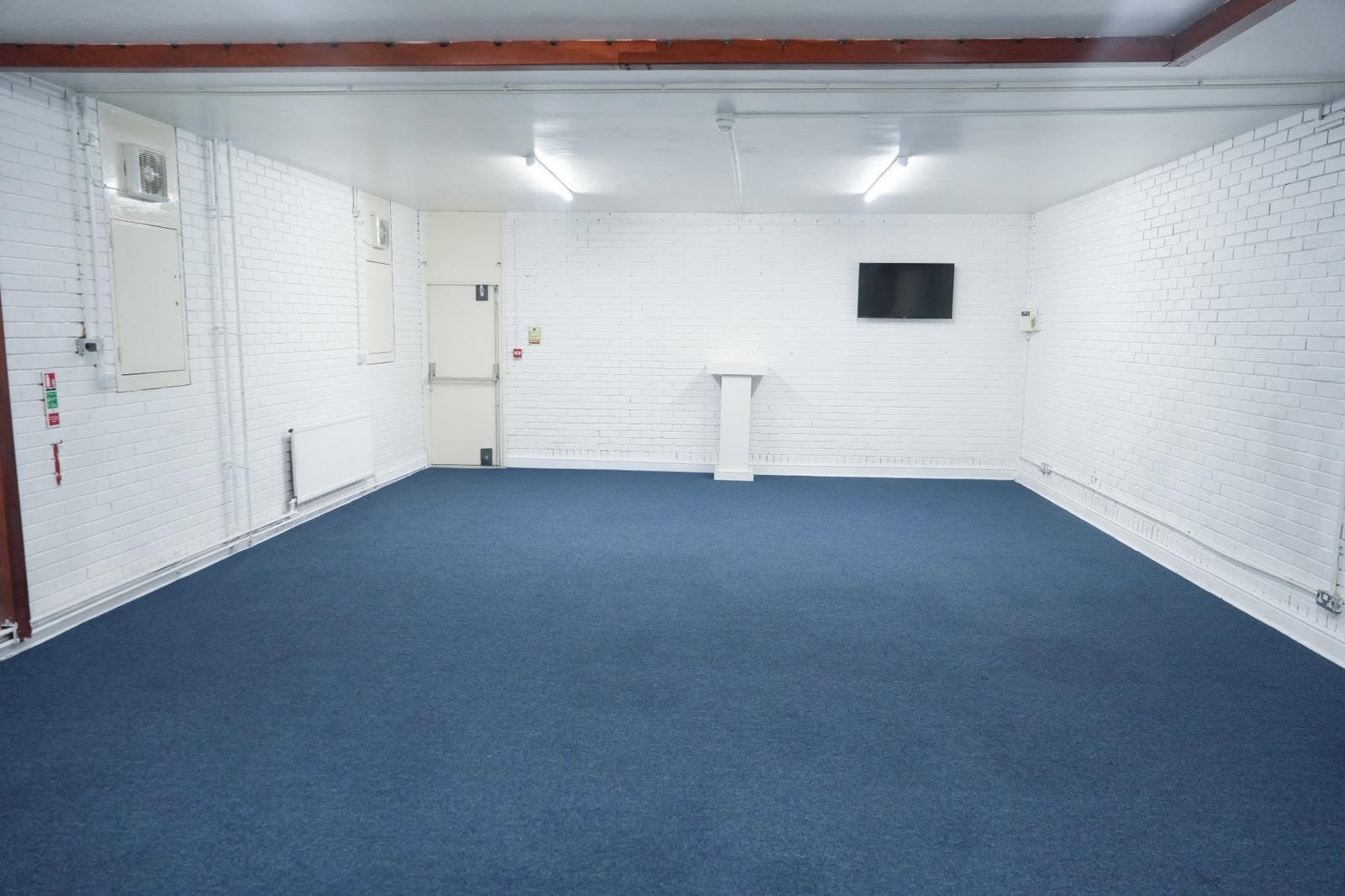 Versatile Canning Town event hall featuring clean blue carpeted flooring, whitewashed brick walls, and a professional lectern.