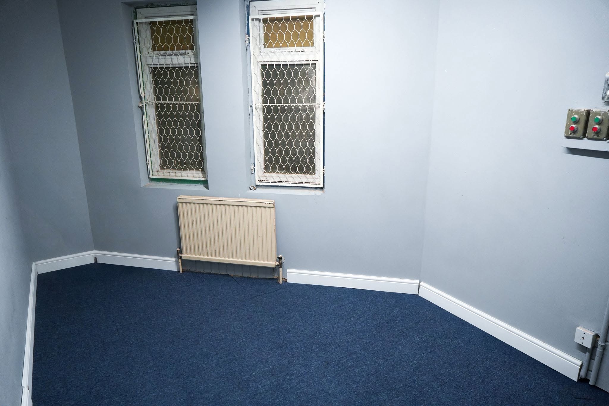 Quiet blank-canvas Canning Town event room with blue carpeted flooring, wall radiators, and opening windows for hire.