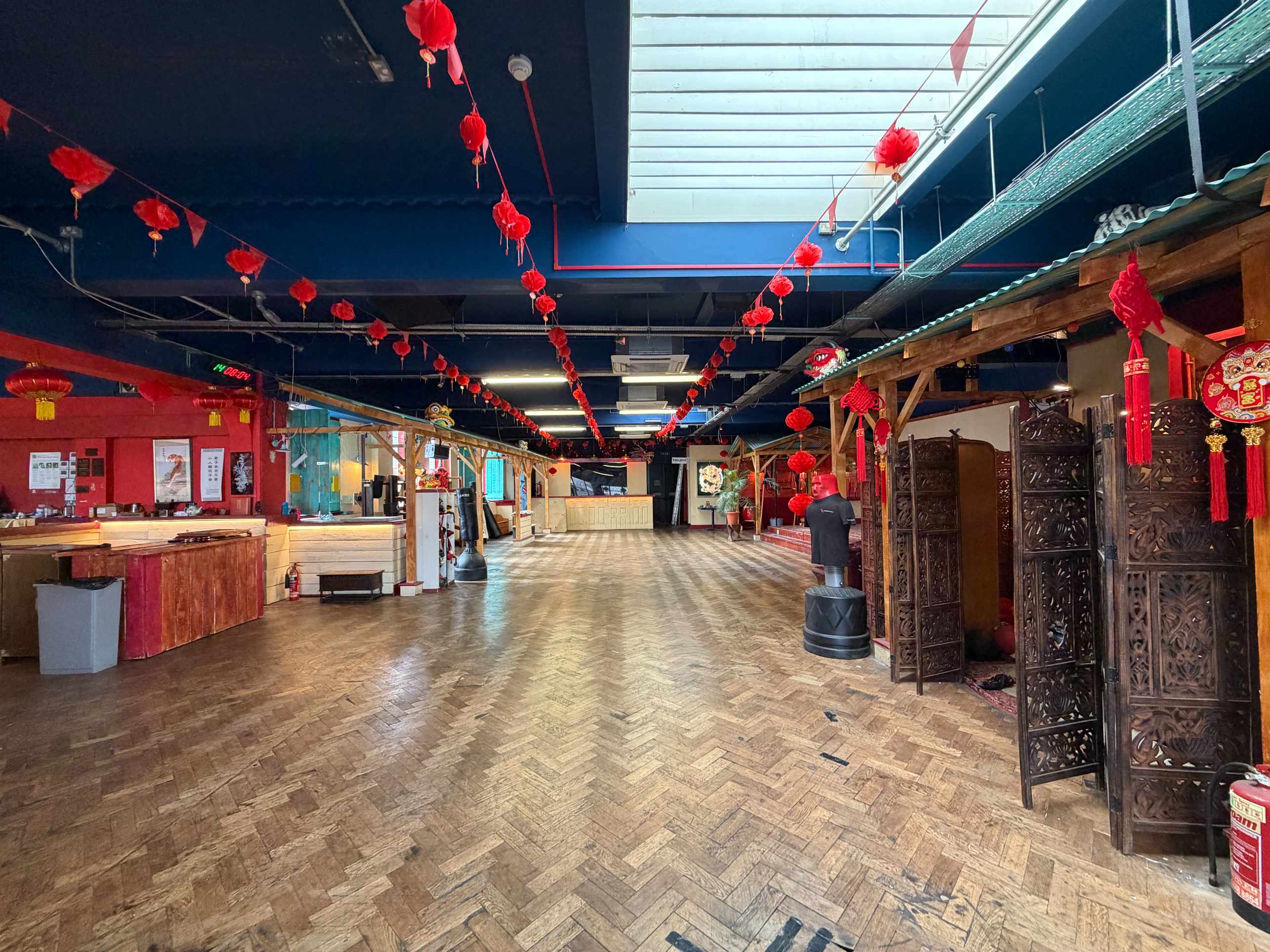 Zhulin Hidden Village hall with pale wood floor, long tables, and Chinese-style red lanterns under a dark ceiling