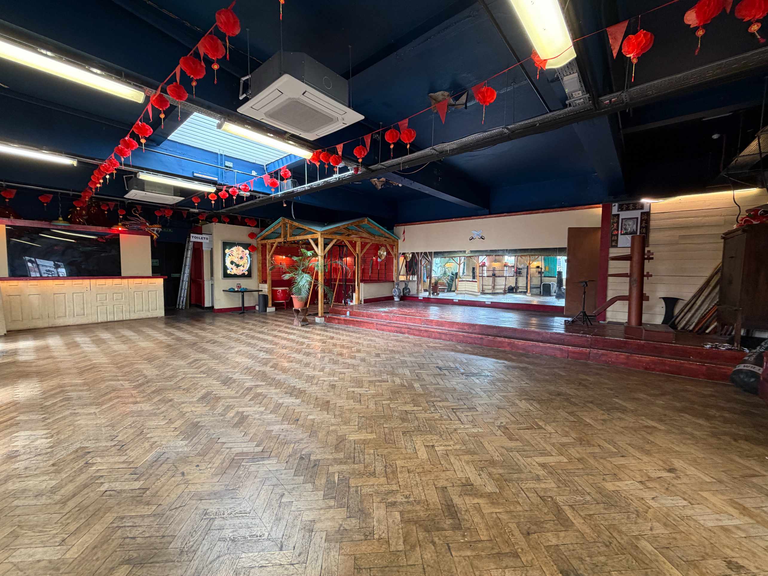 Another view of Zhulin Hidden Village hall with open wooden floor, tables around the perimeter, and red lantern decorations
