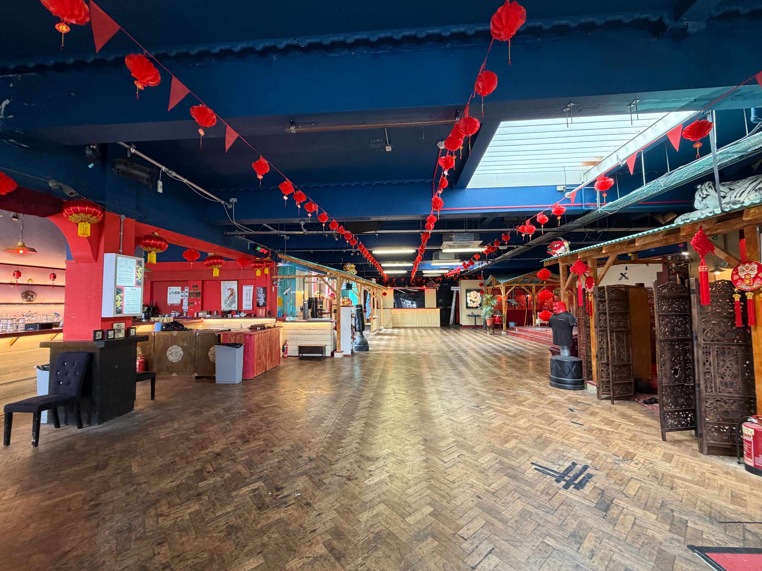 Wide view of Zhulin Hidden Village event hall with pale wooden floor, red lanterns, and seating along the sides