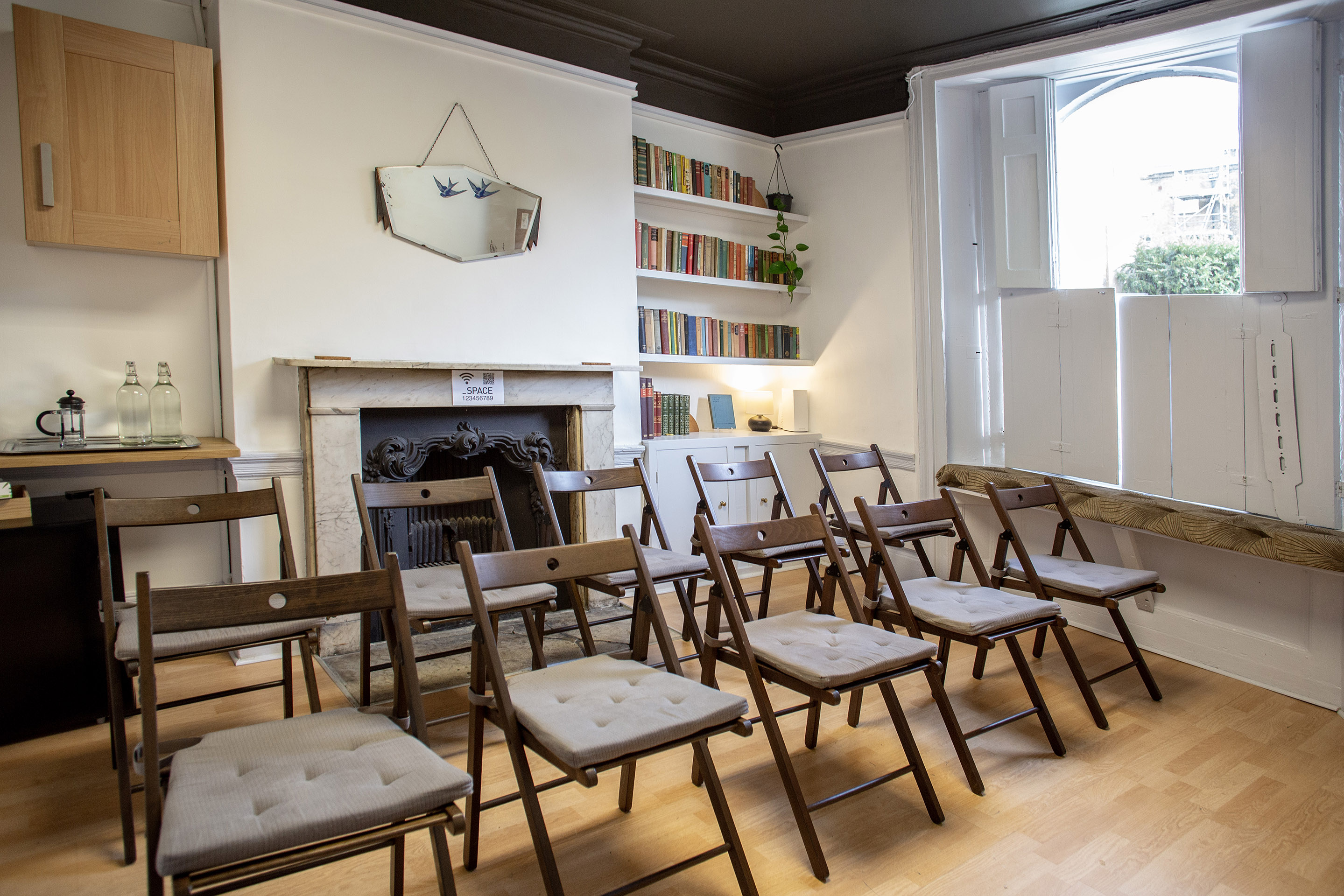 The Study, a versatile London meeting room hire for 10, featuring a round table, bookshelf, and large arched window.
