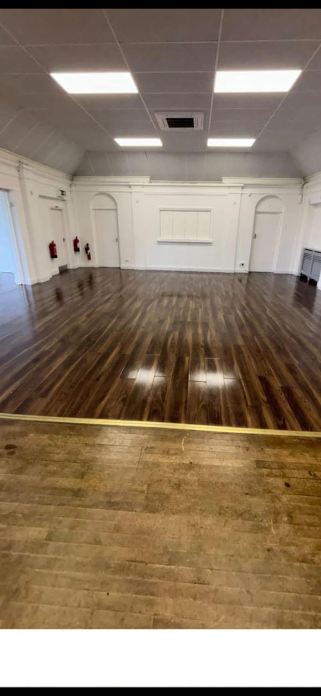 Polished wooden dance floor with a stage in the foreground is visible in an empty hall with white walls and arched doorways.