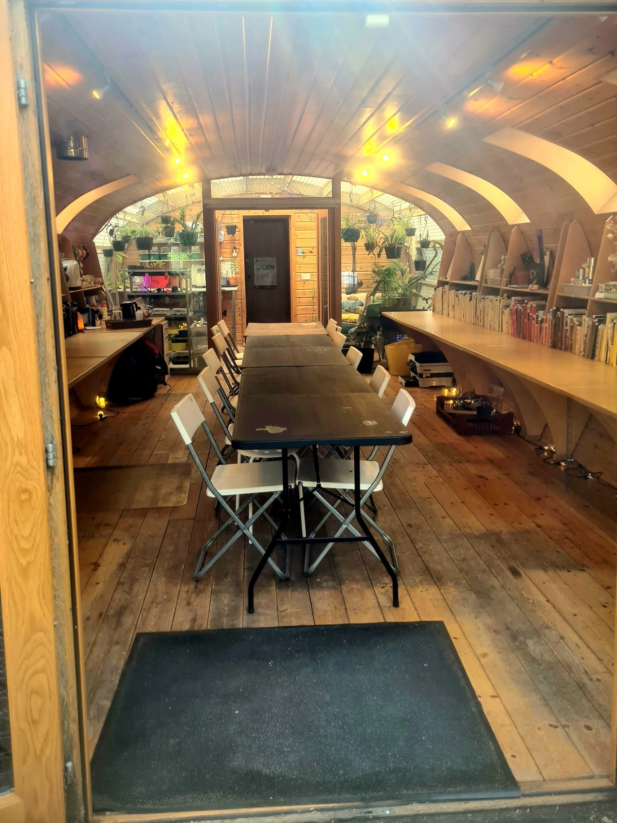 A long, narrow room with a vaulted wooden ceiling, a central table with white folding chairs, and shelves full of books.