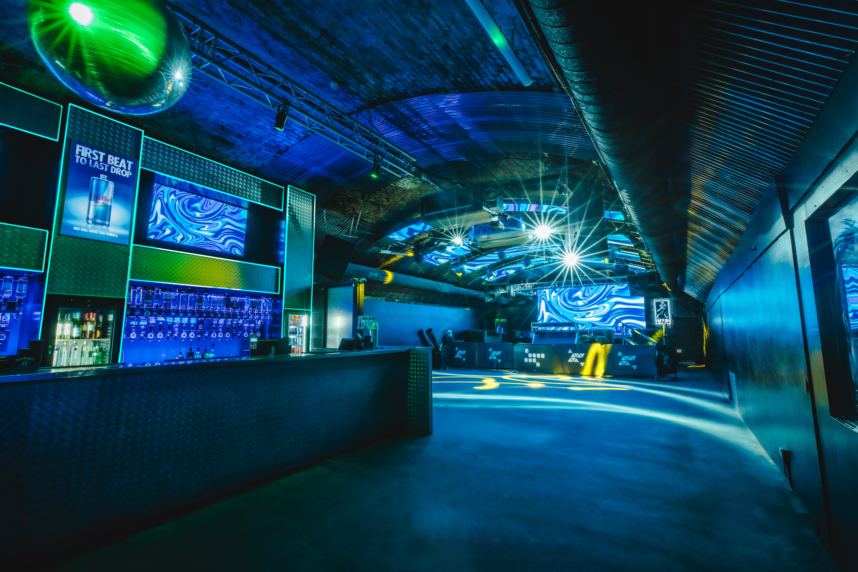 The Fire Main Room at Vauxhall Arches for 600, set with long picnic tables under a large abstract LED screen and blue lighting.