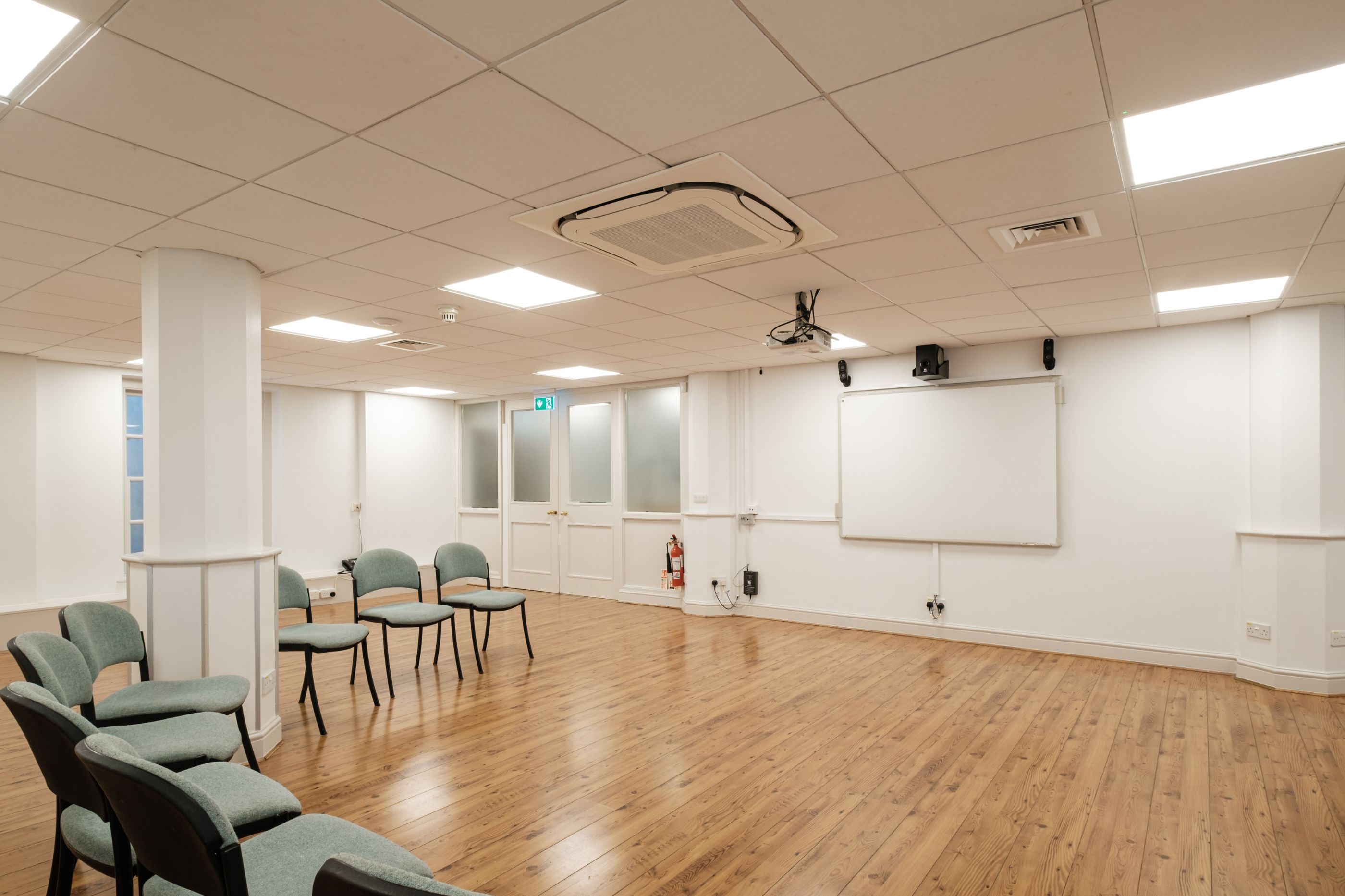 Well-lit meeting room with wood floor, whiteboard, projector, and semi-circle chairs, available to book via Conveenie.