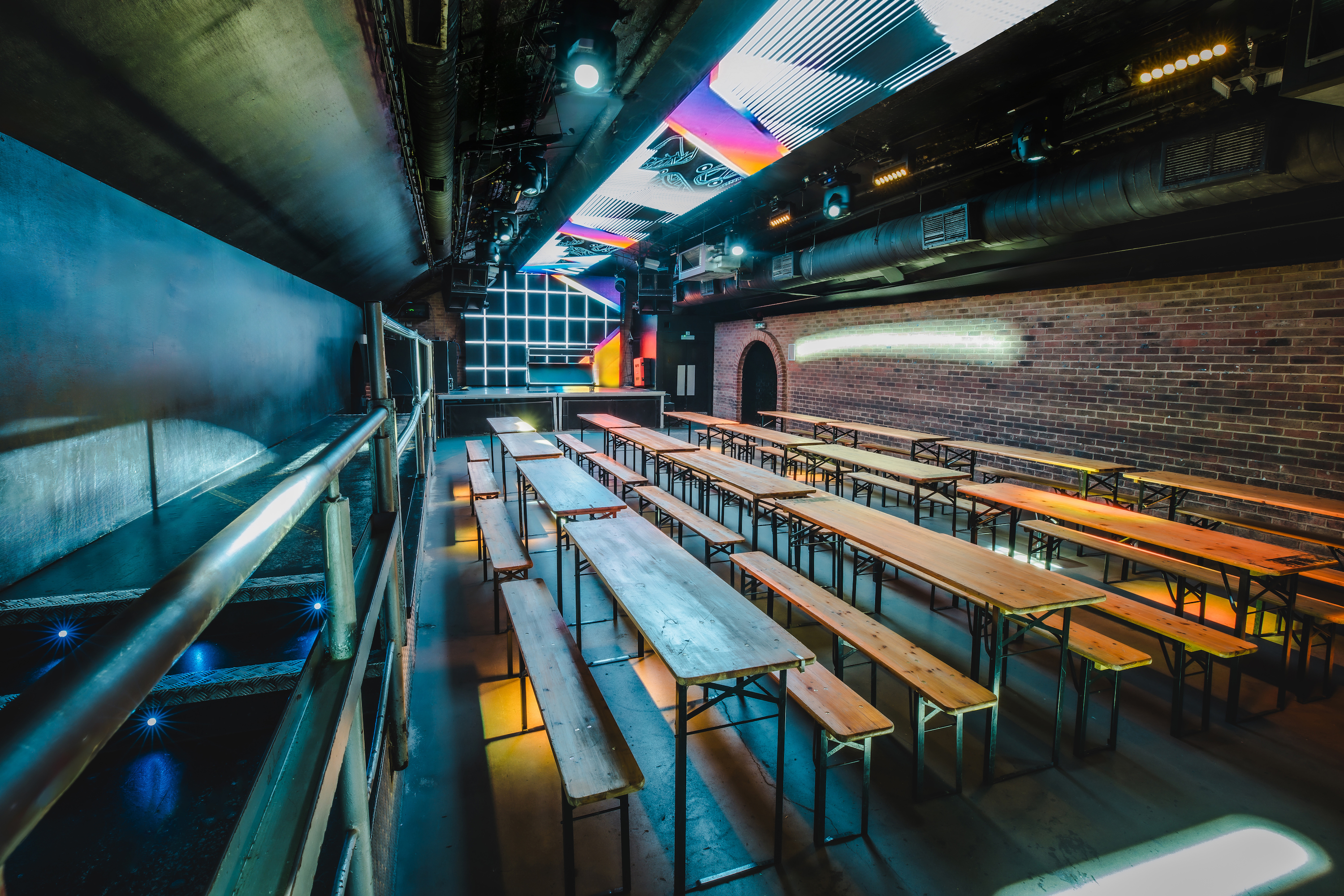 A futuristic nightclub room at Vauxhall Arches, a 600-capacity venue, features a long bar, DJ booth, and disco ball under neon purple light.