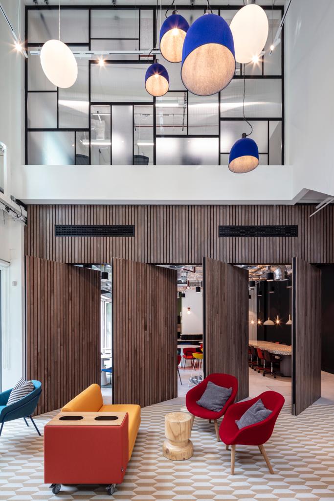 ChatGPT said:  The Lounge at Melanin Health & Wellness, for 40, with wood-slatted doors, high ceilings, pendant lights, and colorful furniture.