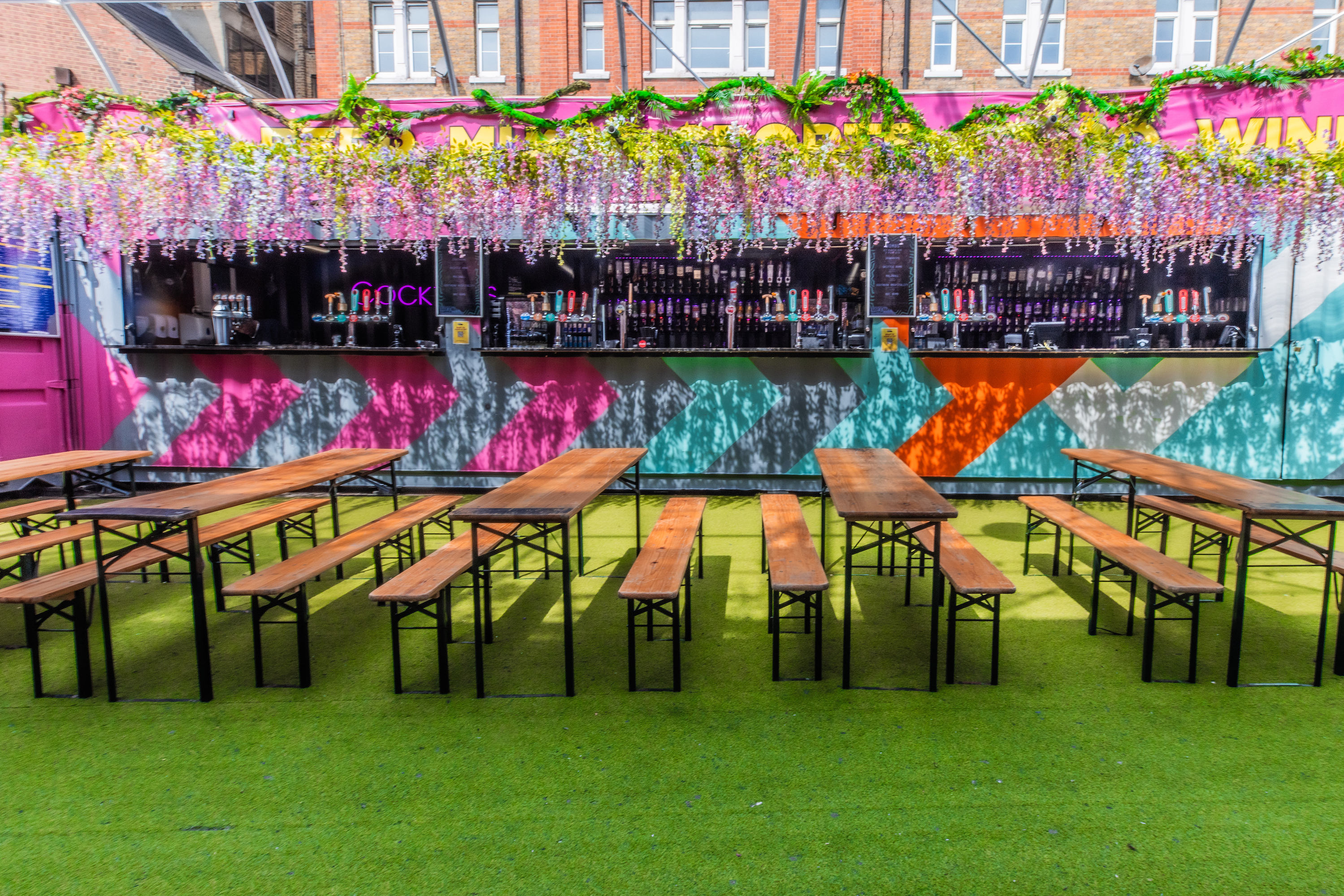 An elevated view of the 800-capacity Vauxhall Food and Beer Garden, showing its long layout under an arched frame, with London skyscrapers towering ab
