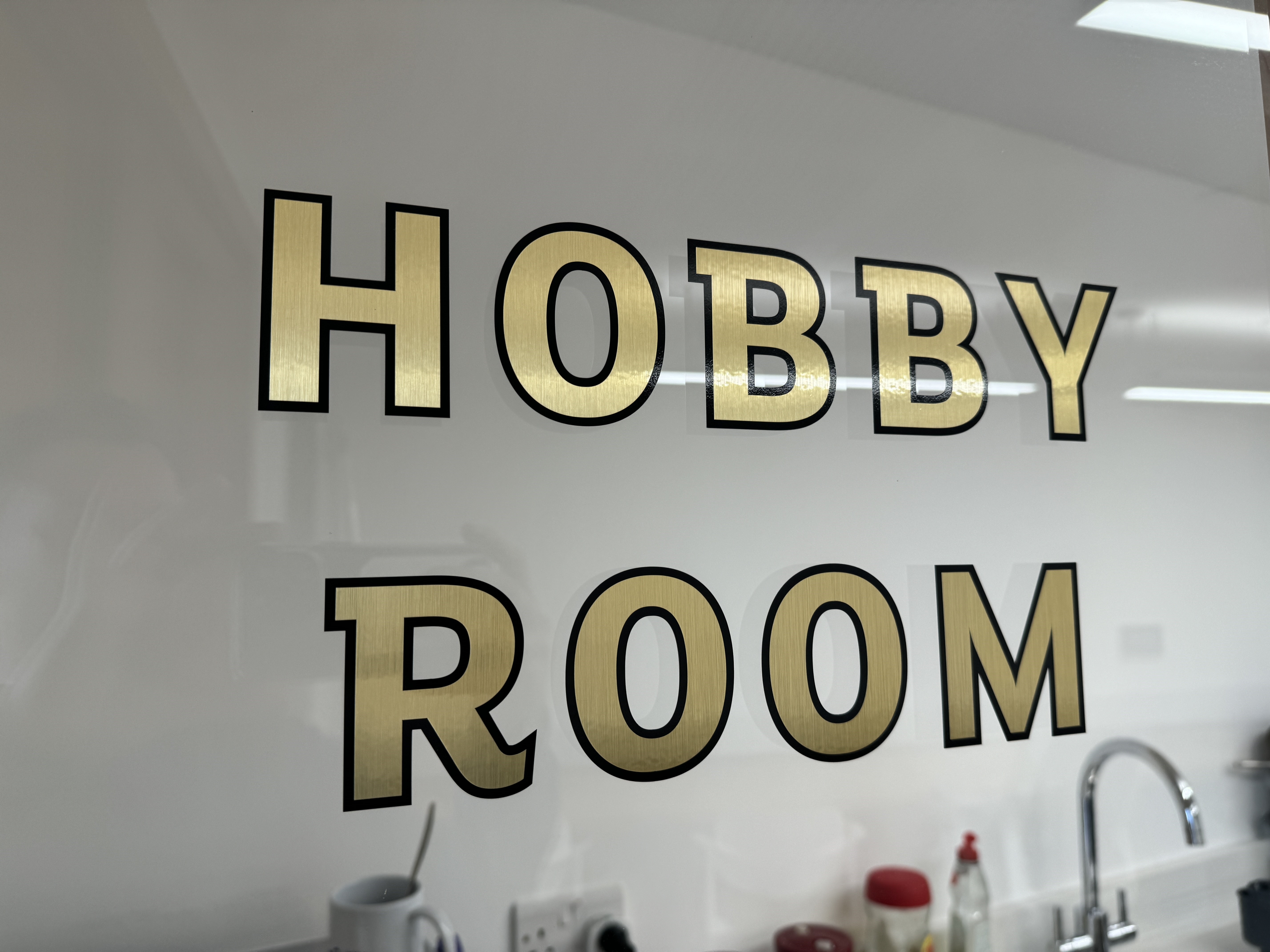 Gold signage for the Hobby Room at Appleby Blue in London, indicating a versatile room hire in London space with a sink and counter.