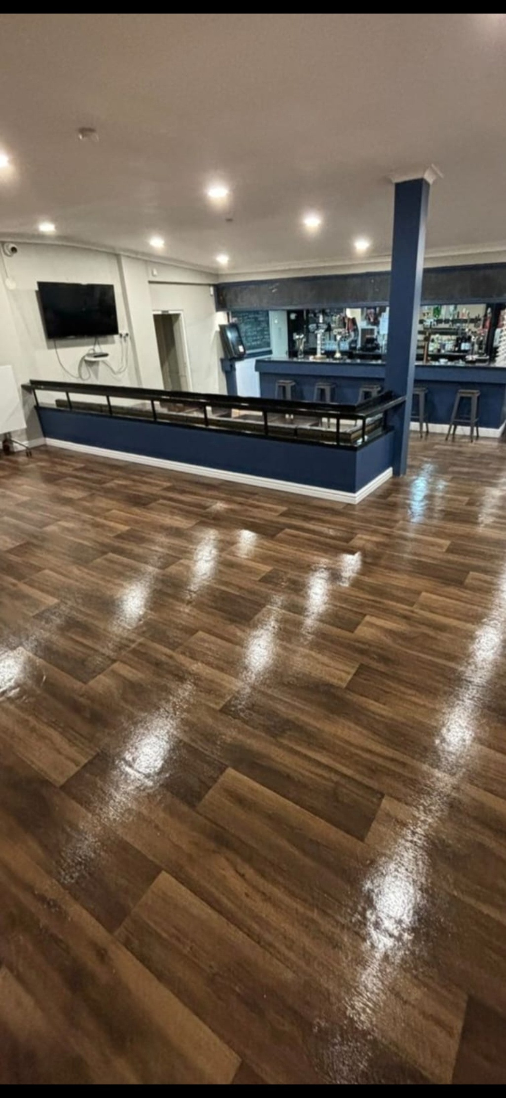 A shiny wood-look floor, a large wall-mounted TV, and a raised section with a dark blue bar - available via Conveenie.