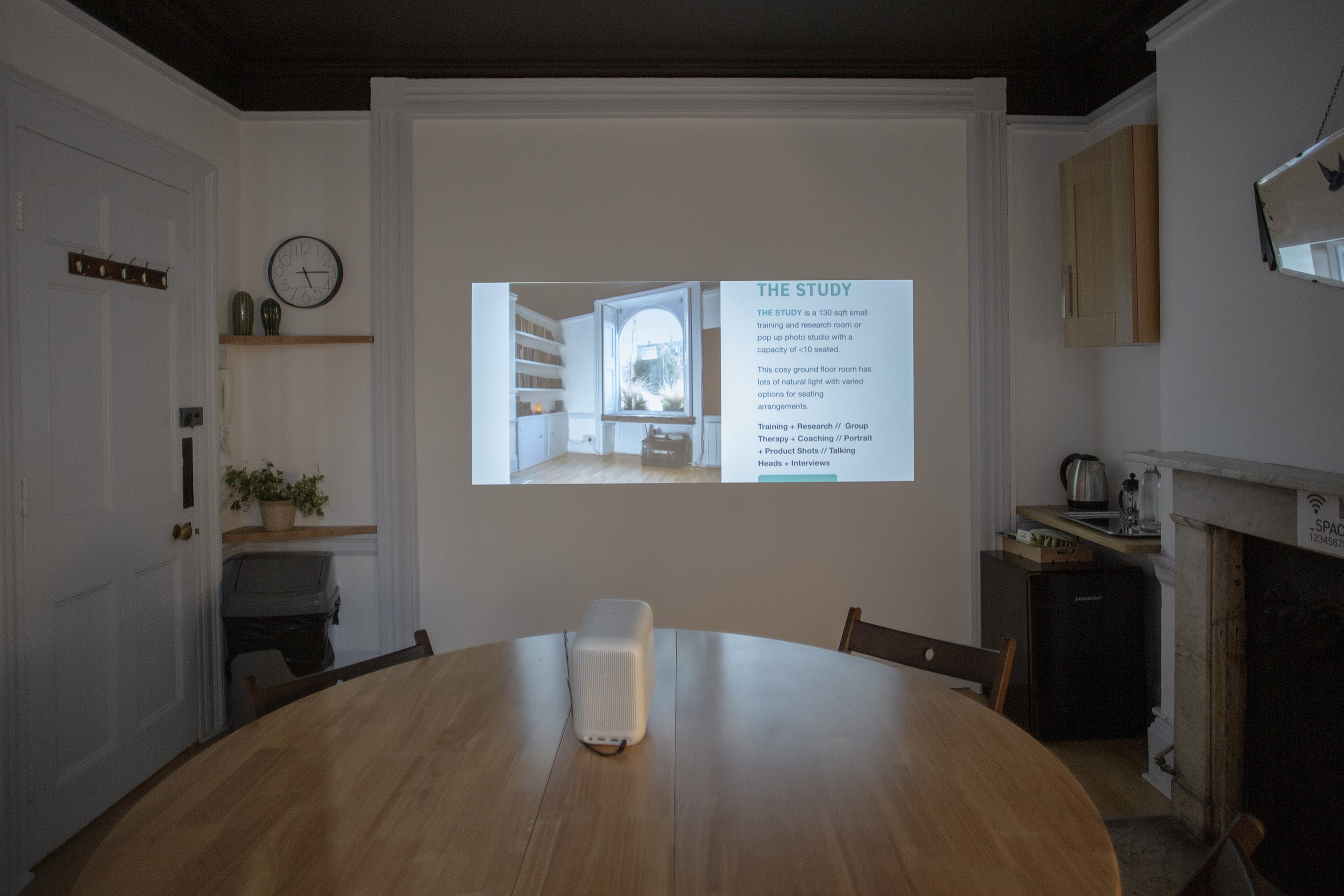 A small meeting room for 10, featuring a round table, projector screen, and a small kitchenette.