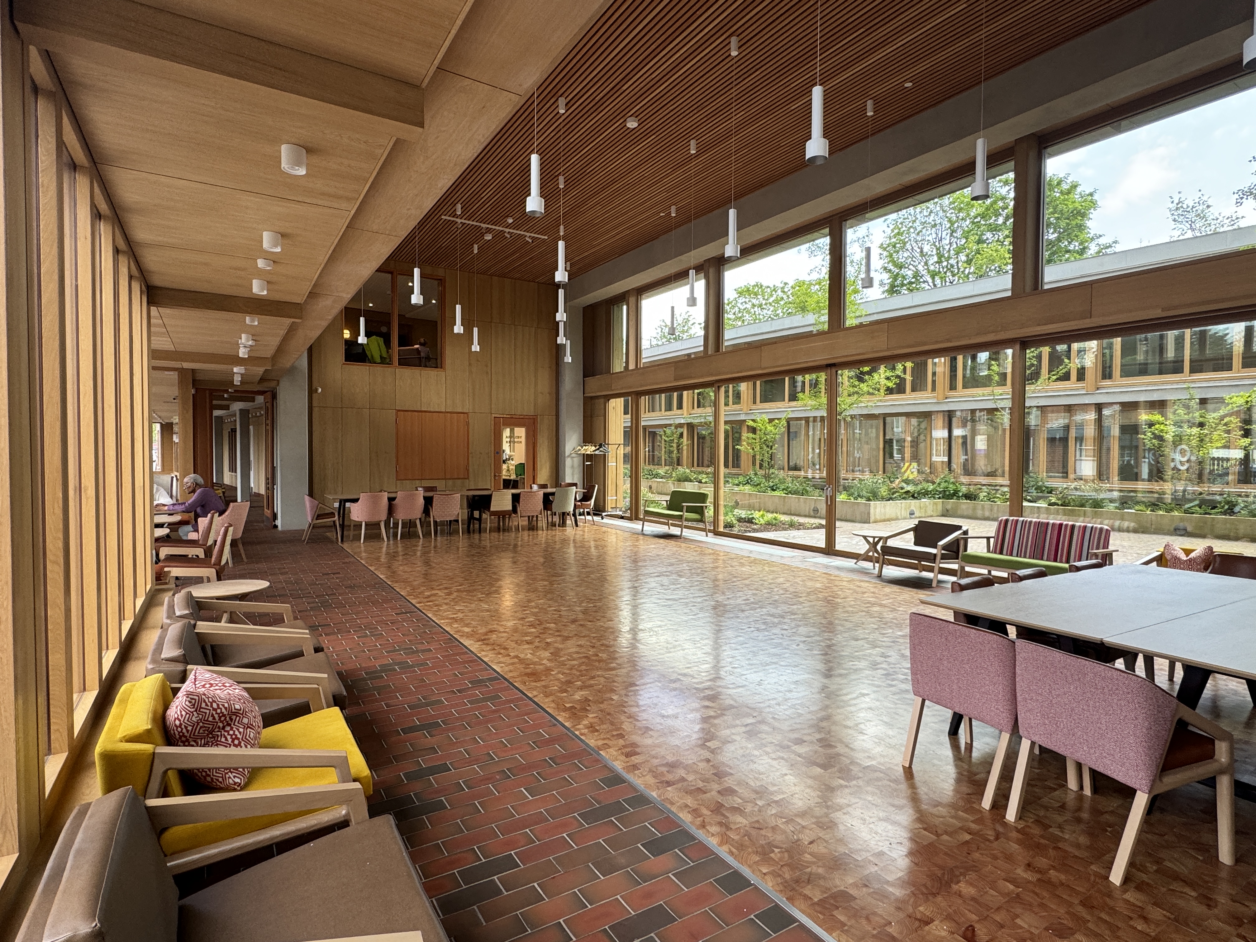 A wide view of The Garden Room at Appleby Blue for 100, showcasing its high, wood-slatted ceiling, spacious parquet floor, and floor-to-ceiling window