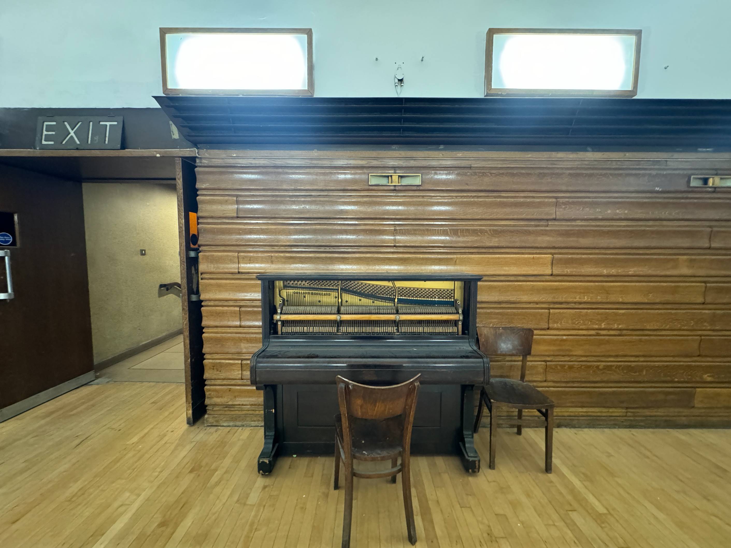 A close-up of an upright piano standing against the wood-panelled wall of the Minor Hall.