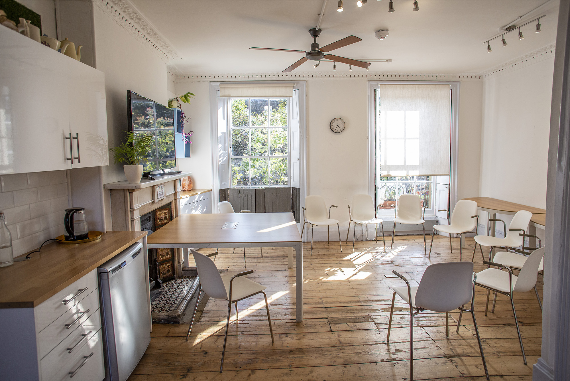 Bright meeting room hire in London at The Office, Anomalous Space, featuring a kitchenette, ceiling fan, and wooden floors for 15 guests.