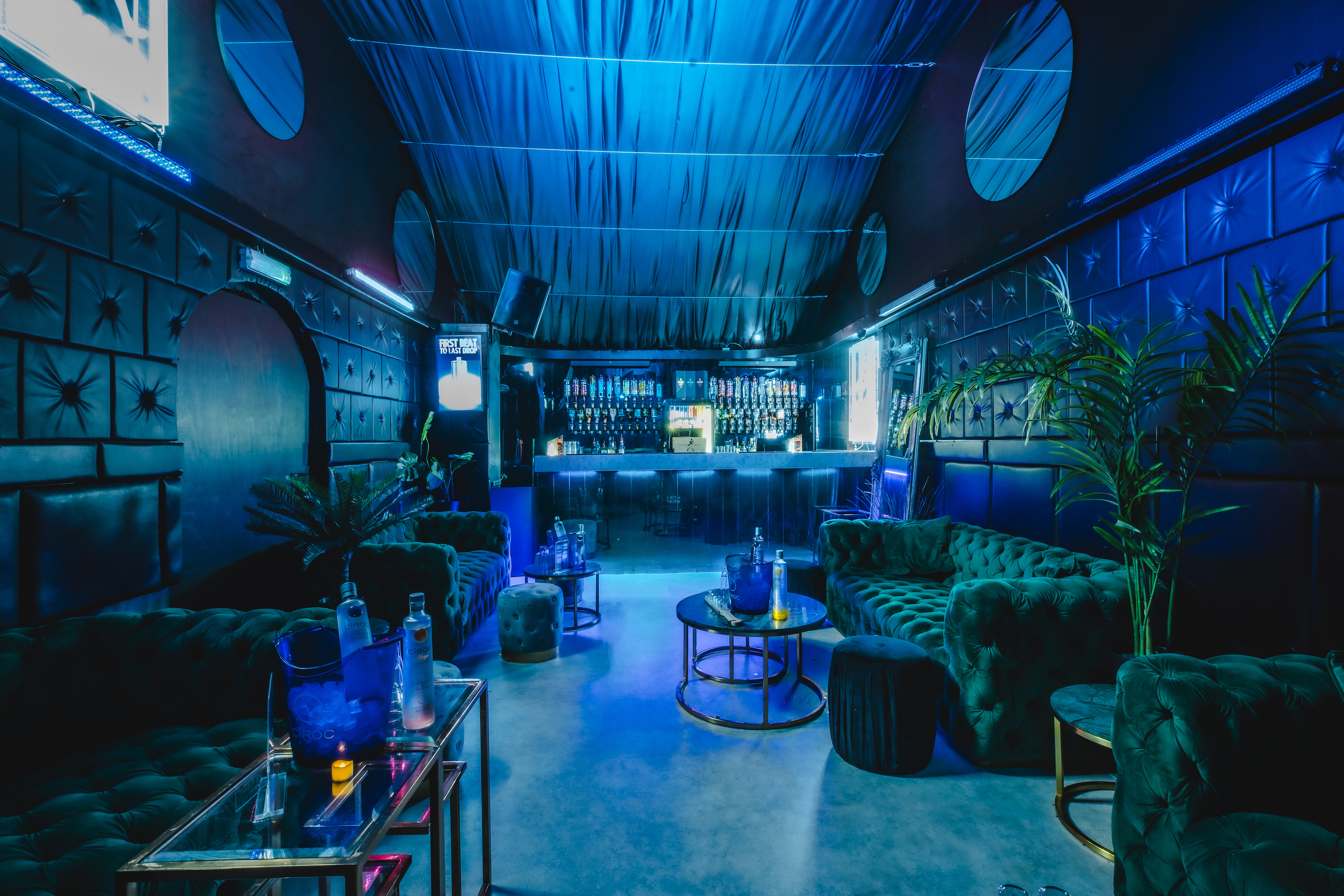 A stylish bar at Vauxhall Arches, a 600-capacity venue, features an exposed brick front with arches, illuminated by cool blue and pink lights.