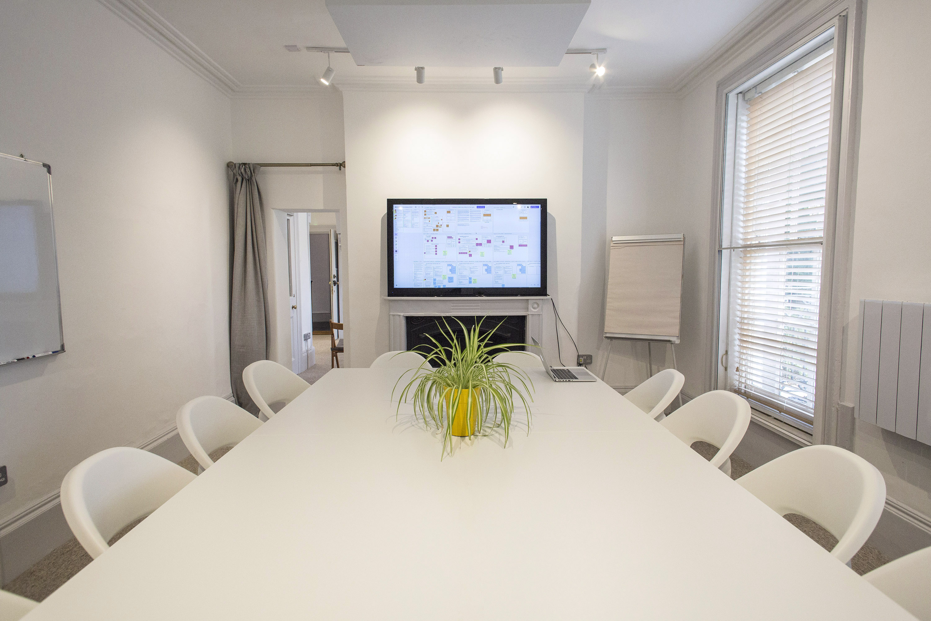 Modern meeting room hire in London at The Flat, Anomalous Space, featuring a clean white table, TV screen, and whiteboard for efficient collaboration.