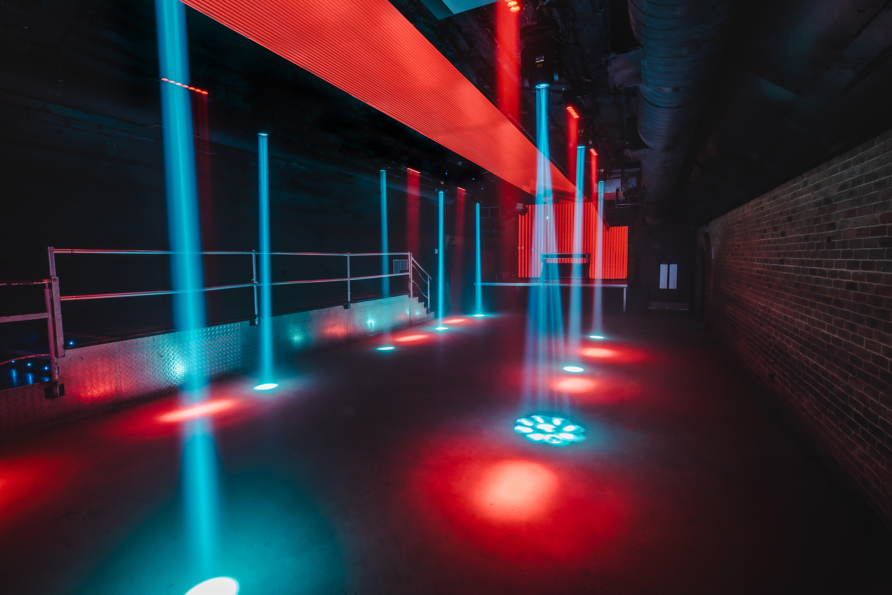 The empty Fire Main Room at Vauxhall Arches, a 600-capacity club space listed on Conveenie, is lit with dramatic red and blue spotlights.