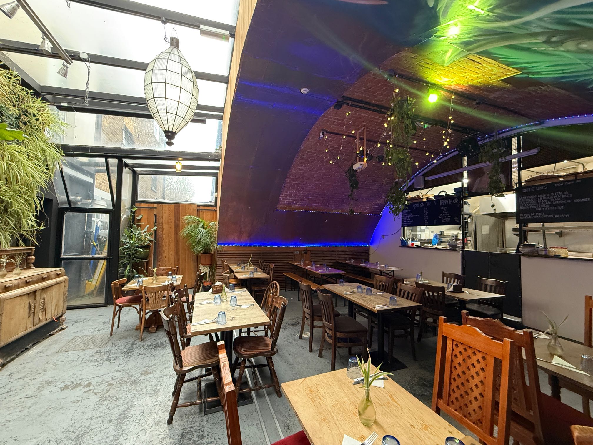 A vibrant restaurant with wooden tables and chairs, a vaulted brick ceiling, a glass roof, and a large white lantern - available to book via Conveenie
